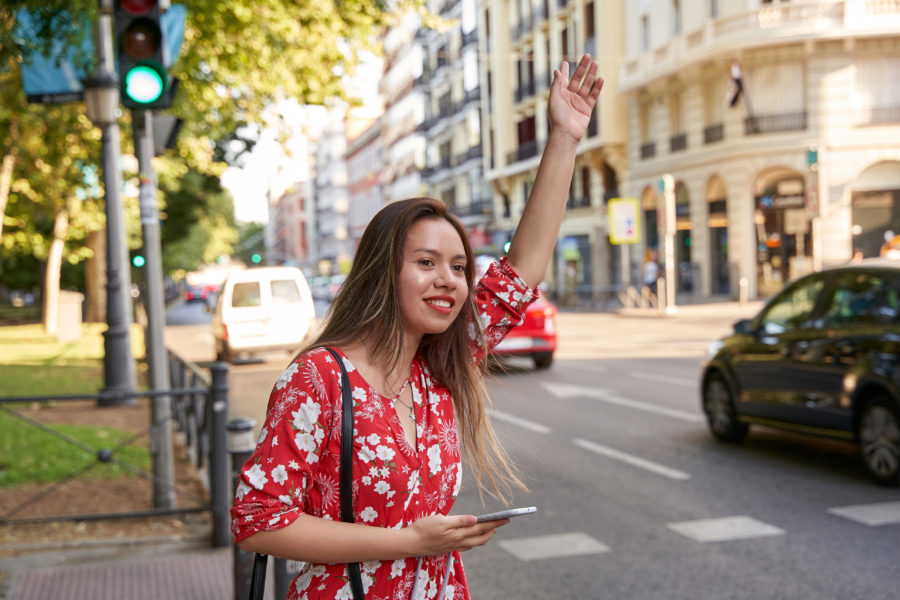 Young woman on the street and raising arm to call to attention of a cab. She is holding a smart phone on her other hand. Concept of taxi application