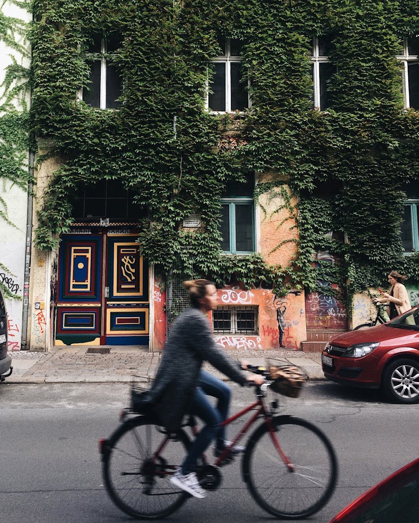 Person Riding on Bicycle Beside Concrete House With Green Vines