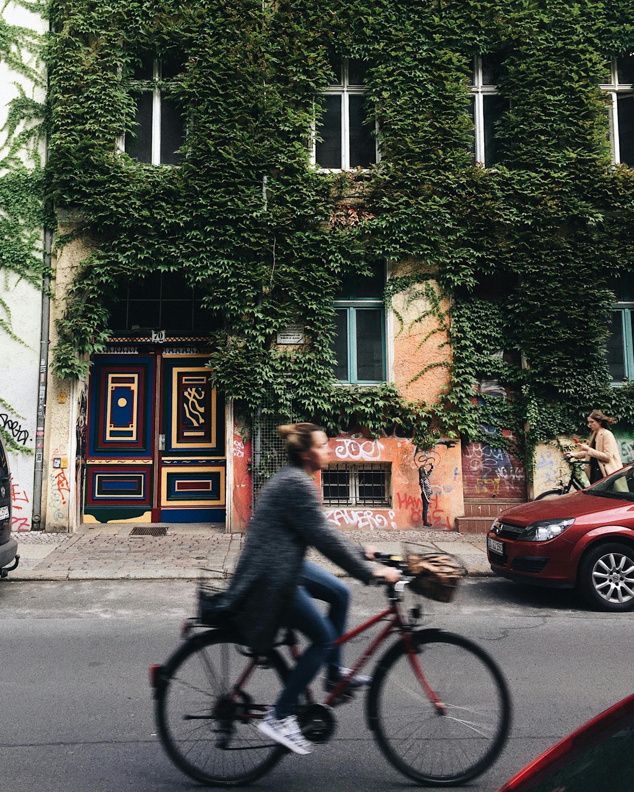 Person Riding on Bicycle Beside Concrete House With Green Vines