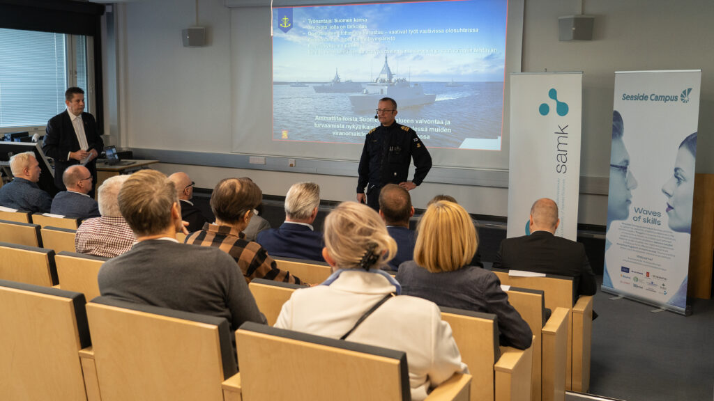 A seminar speaker in the seminar hall with lots of people in the audience.