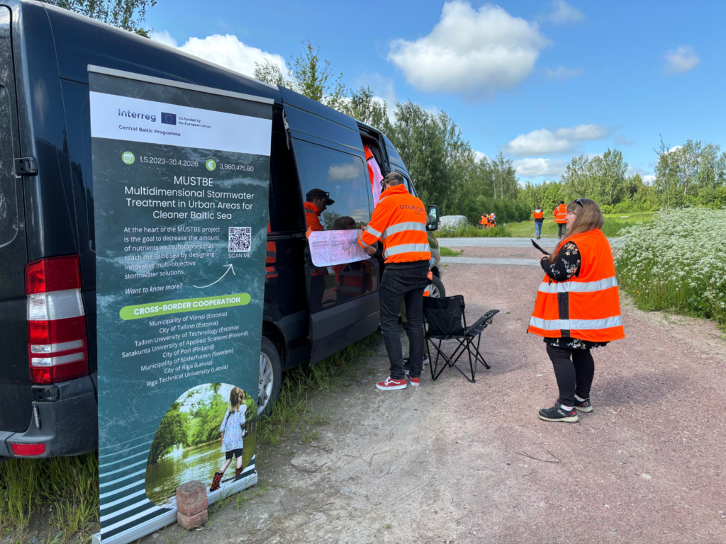 The MUSTBE rollup in front of a van and some volunteers at the Pori wetland pilot site event.