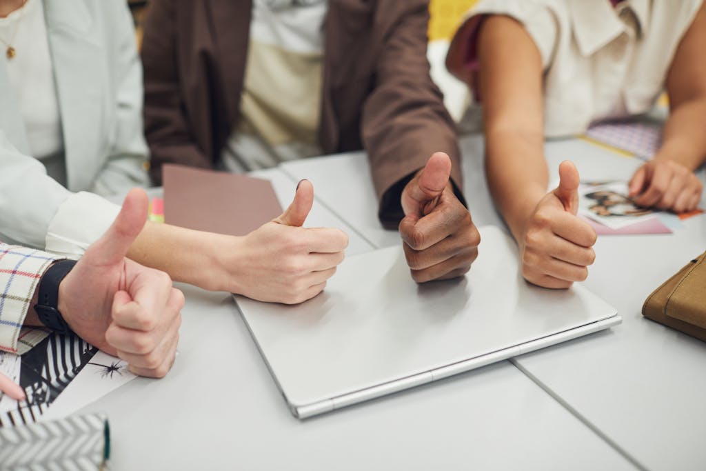 Four diverse hands showing thumbs up over a laptop on a desk, symbolizing teamwork and approval.