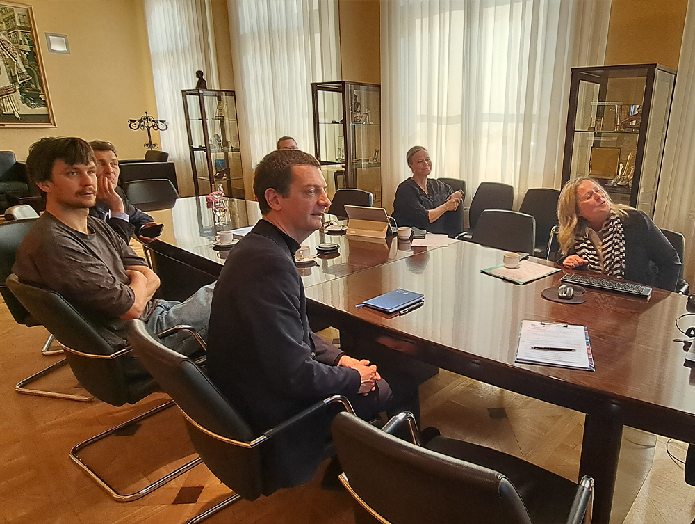 A group of people sitting around a long wooden table during a meeting in a formal conference room.