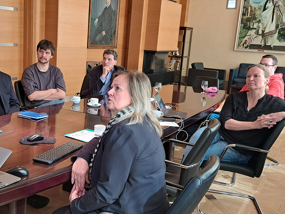A group of people sitting around a long wooden table during a meeting in a formal conference room.