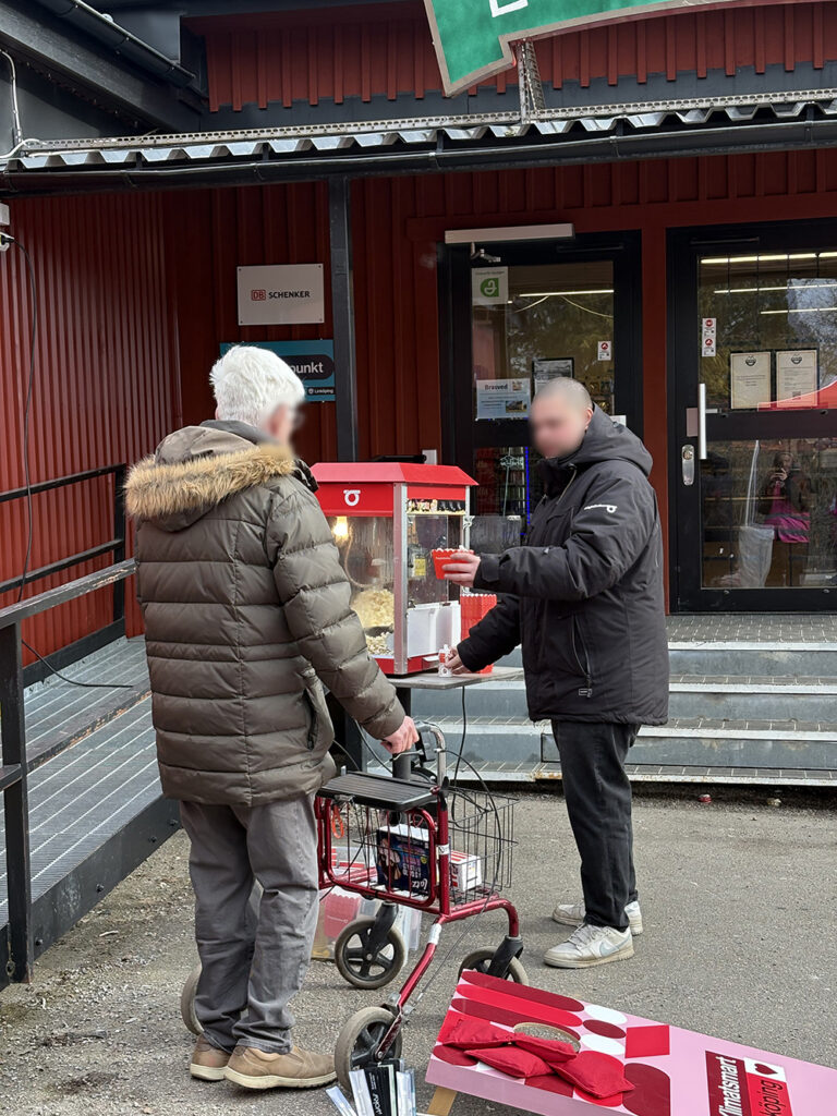 A man serving popcorn from a red machine to an elderly person using a walker outside a red building.