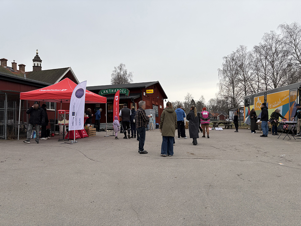 An outdoor community event on a cloudy day with a red tent, a village store, and a mobile library bus parked in the background.