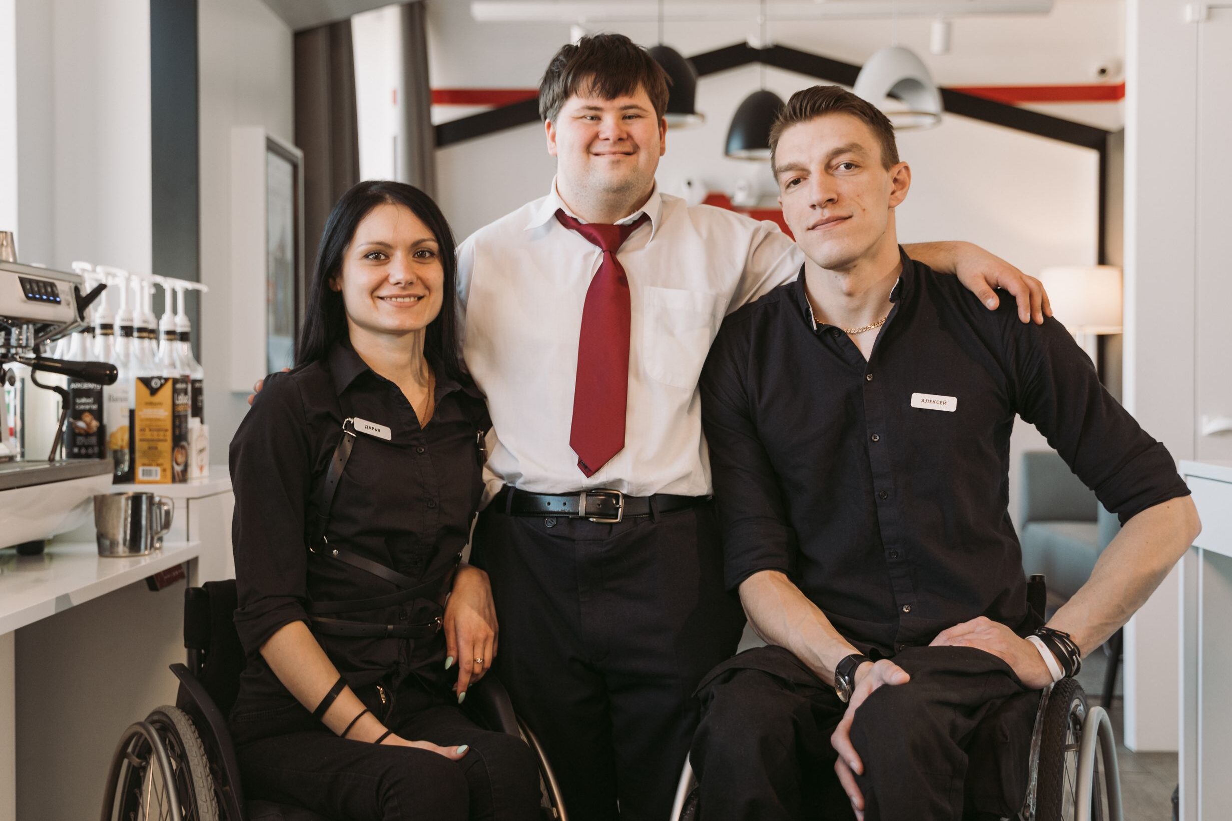 A group of diverse adults, including those in wheelchairs, smiling in a cafe environment fostering teamwork.