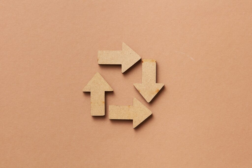 Wooden arrows arranged in a circle on a beige background, symbolising the circular economy and the continuous reuse of resources.